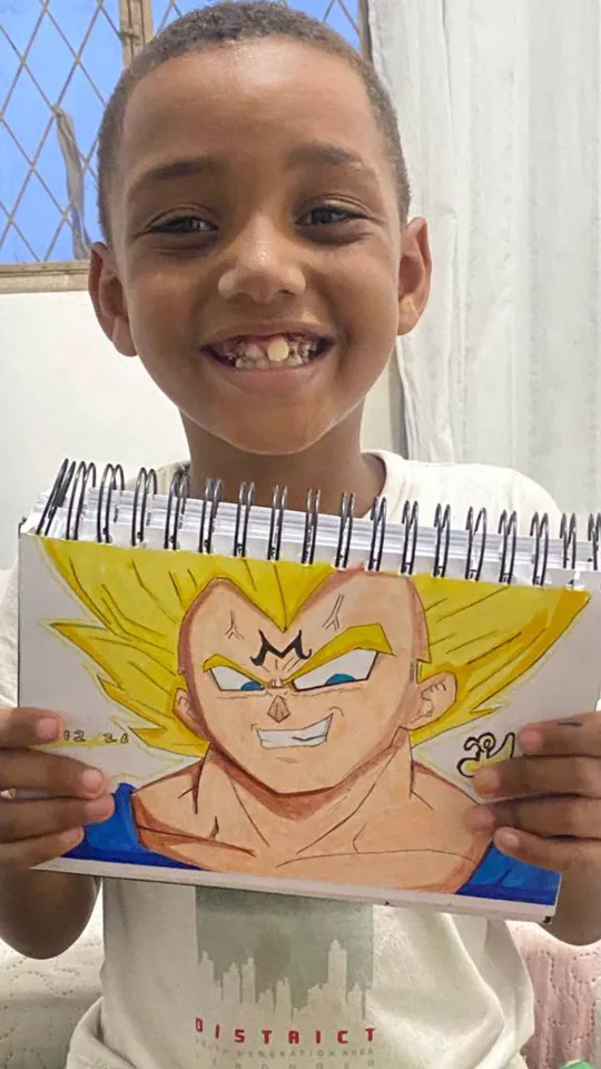 Menino sorrindo mostrando o desenho do Vegeta, de Dragon Ball, feito na aula ao vivo