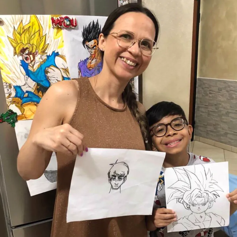 Juliana Oliveira sorrindo ao lado do filho Arthur, os dois segurando desenhos feitos por ele