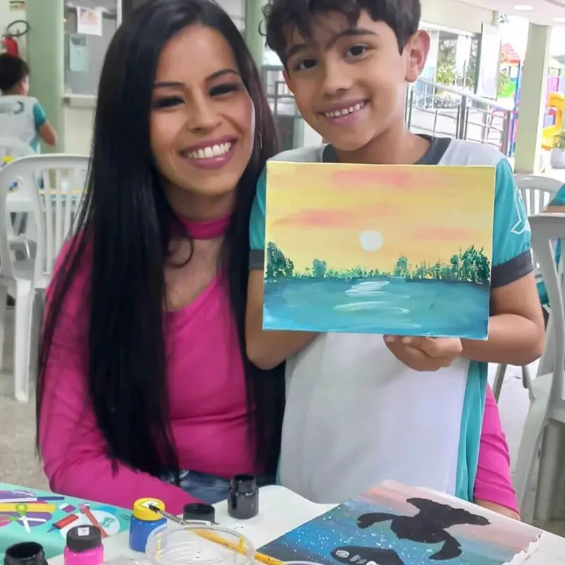 Fabiana Reis e o filho Cézar segurando uma pintura de paisagem feita por ele