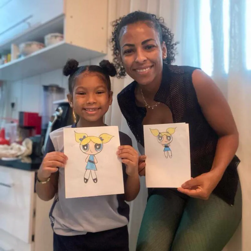Ana Lima e a filha Tereza mostrando desenhos coloridos das Meninas Superpoderosas
